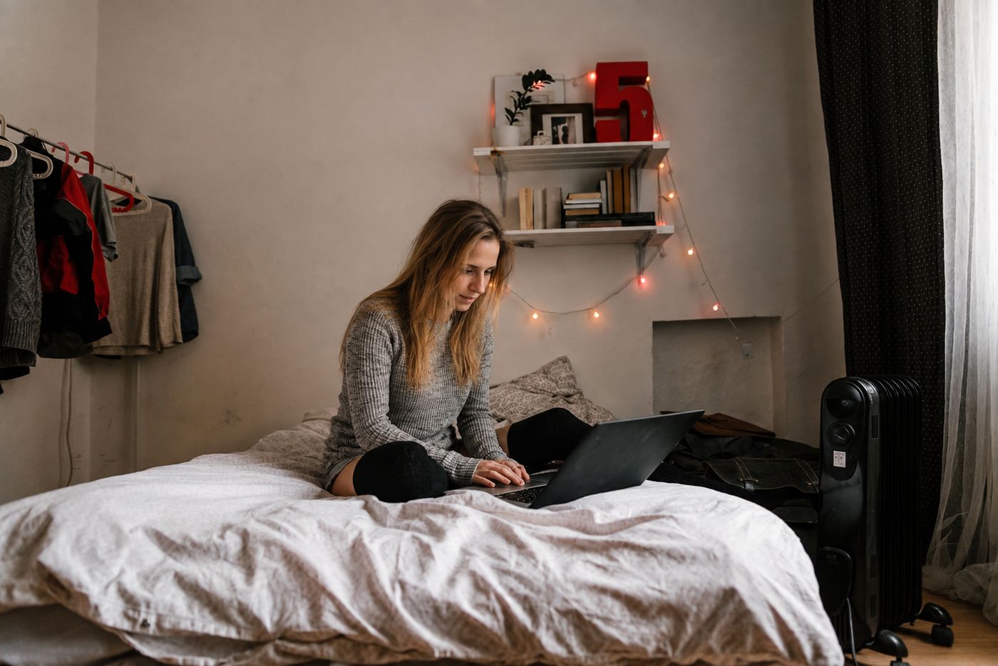 A woman on her bed with a laptop in a cosy room