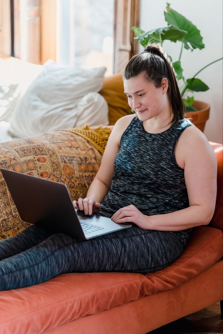 A woman smiling at her laptop on a sofa at home