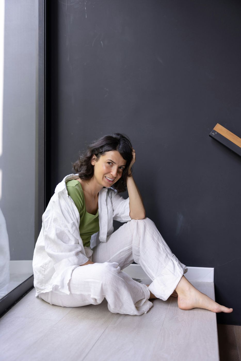 A smiling woman in a white outfit sitting against a dark wall